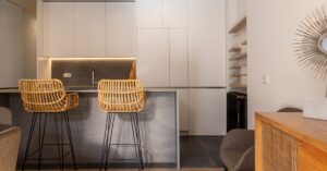 Stylish minimalist kitchen in Madrid featuring sleek design and rattan chairs.